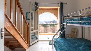 A room with a bunk bed, wooden staircase, and a view through an open door to a balcony.