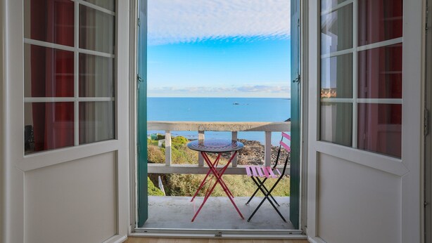 An open door leading to a balcony with a view of the sea, a round table, and two chairs. - Studio "Direct Sea View for 2 People" with Sea View, 2 Balconies and Wi-Fi (Saint-Quay Portrieux)