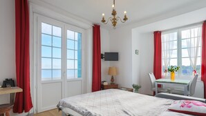 A hotel room with a bed, desk, chair, TV, and a window with curtains. - Studio "Direct Sea View for 2 People" with Sea View, 2 Balconies and Wi-Fi (Saint-Quay Portrieux)