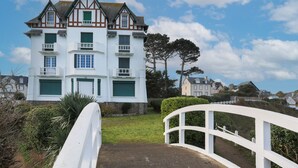 A white building with multiple windows and a balcony, surrounded by greenery and a white fence. - Studio "Direct Sea View for 2 People" with Sea View, 2 Balconies and Wi-Fi (Saint-Quay Portrieux)