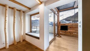 A modern interior with wooden beams, a large window with a mountain view, and a built-in TV.