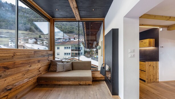A modern interior with a wooden bench, large windows, and a kitchen area.