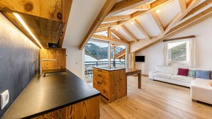 Een moderne keuken met houten balken, een zwart aanrecht en uitzicht op bergen door grote ramen.