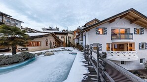 Een hotel met een houten terras, een met sneeuw bedekte zwembad en traditionele Alpenarchitectuur.