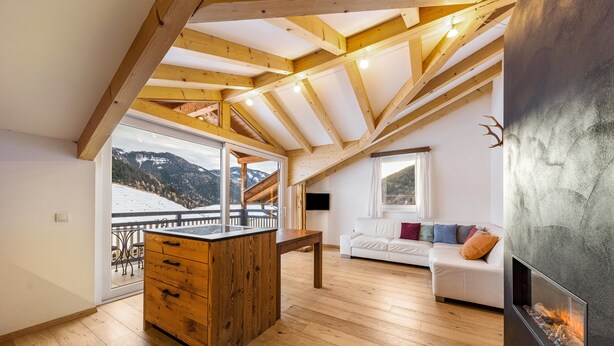 Een ruime loft met een houten plafond, een open haard, een witte bank en uitzicht op met sneeuw bedekte bergen.