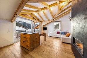 Un loft amplio con techo de madera, chimenea, sofá blanco y vistas a montañas nevadas.