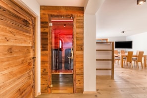 Eine Holztür, die in einen Raum mit roter Beleuchtung führt, mit einem Essbereich mit Holzzimmermöbeln und einem an der Wand befestigten Fernseher.