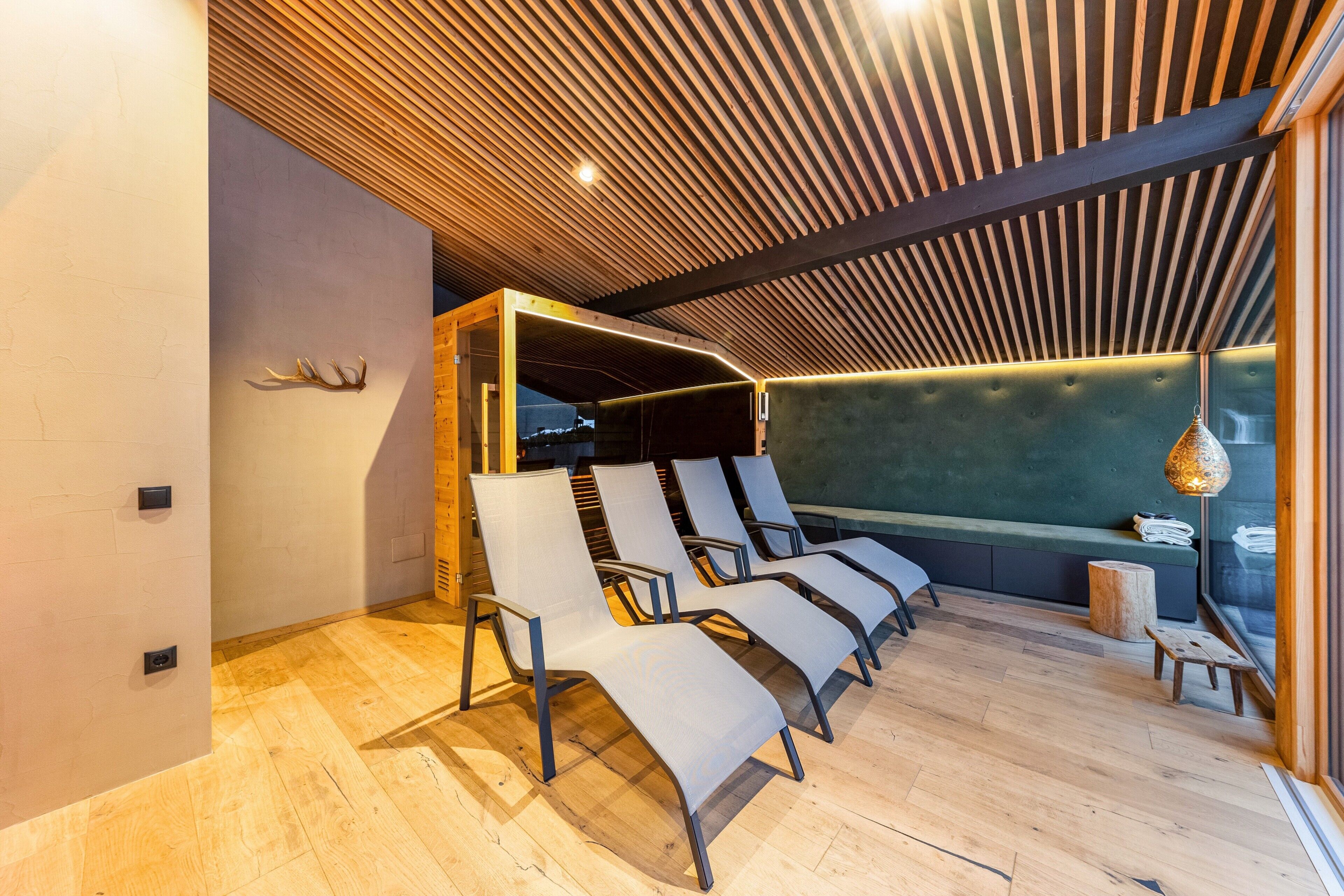 Un interior moderno con techo de listones de madera, un área de estar con sillones acolchados, un banco e iluminación colgante.
