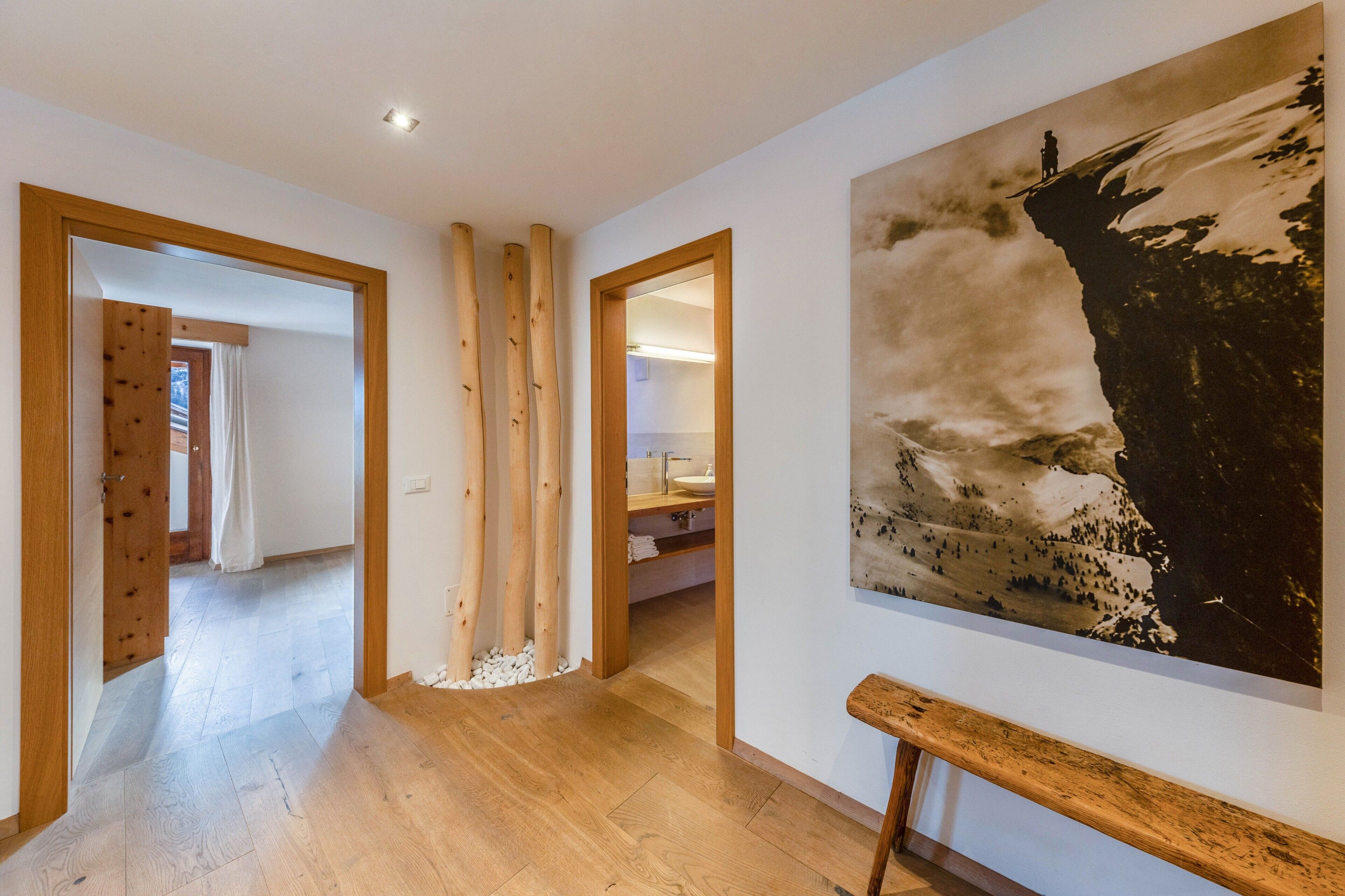A hallway with wooden flooring, a wooden bench, and a large mountain landscape painting on the wall.
