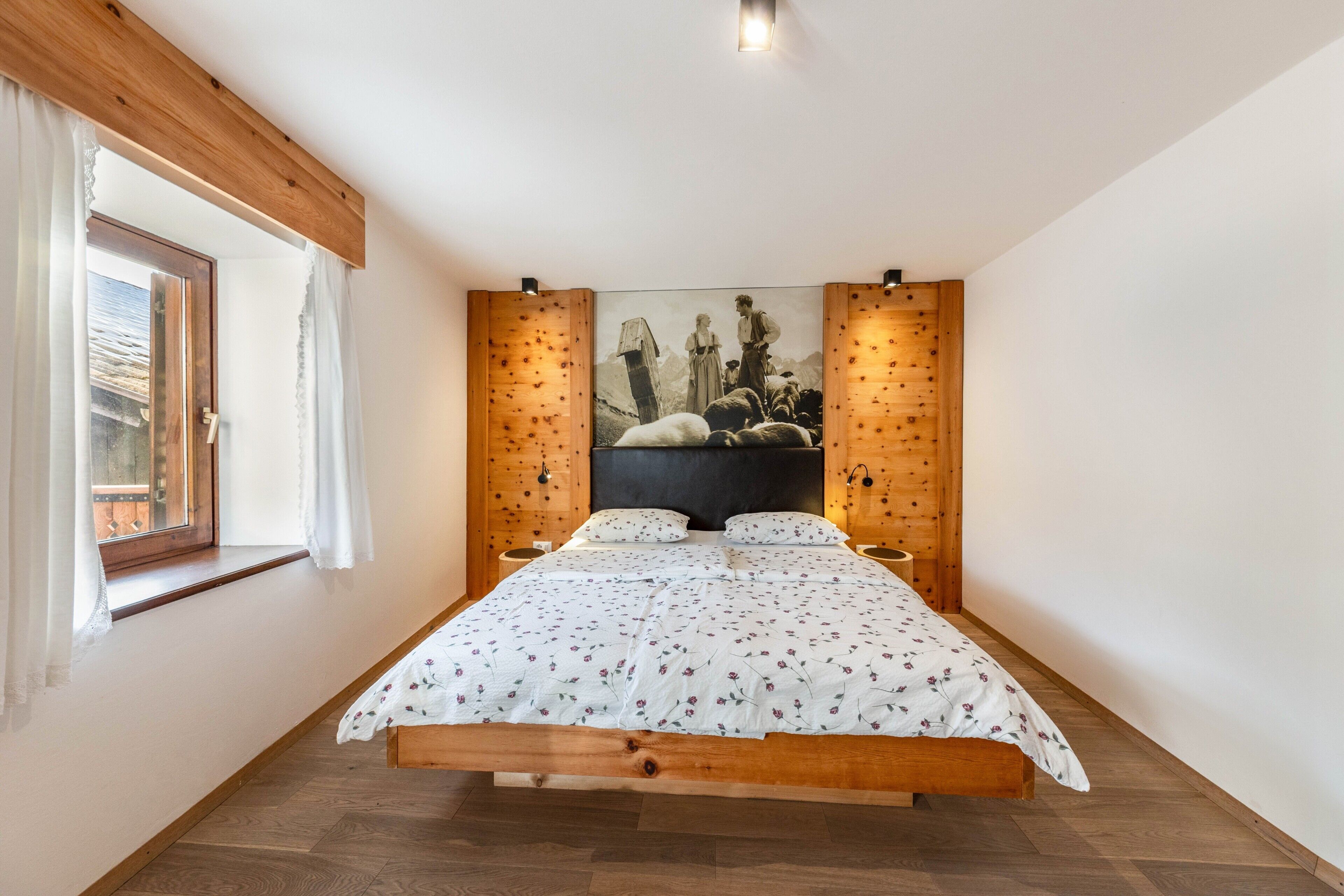 Une chambre avec un lit en bois, une fenêtre avec des rideaux, un tableau au mur et un plafond en bois.