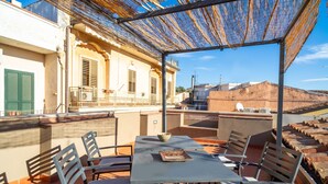 A rooftop terrace with a table and chairs, a pergola, and a view of buildings in the background.