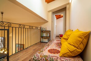 Un couloir avec un tapis à motifs, une bibliothèque et un coussin jaune.