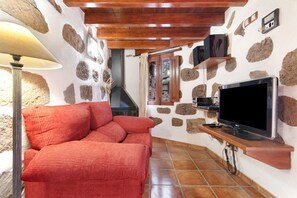 Una habitación acogedora con un sofá rojo, televisión y paredes de piedra.