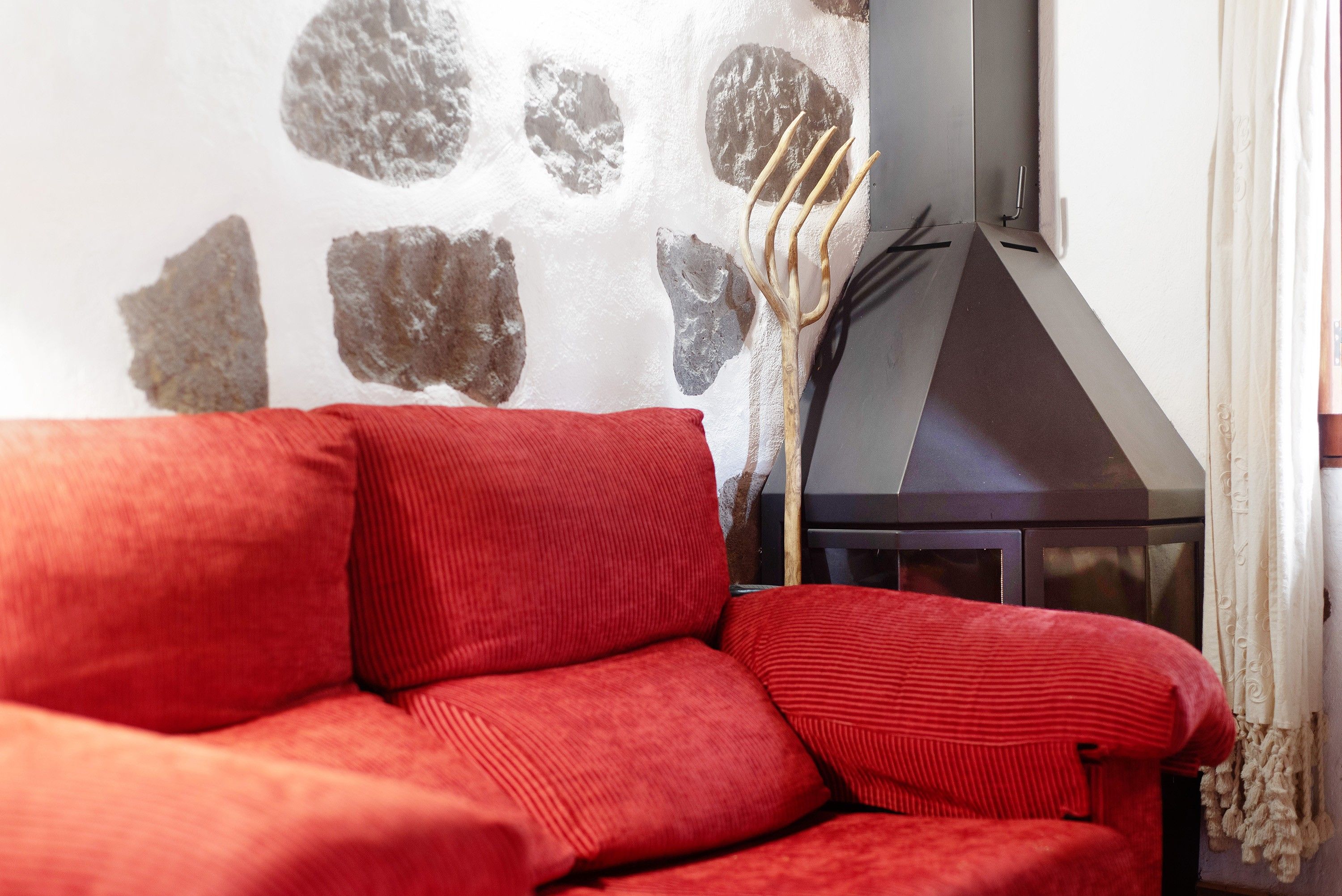A red sofa in a room with a stone wall and a fireplace.