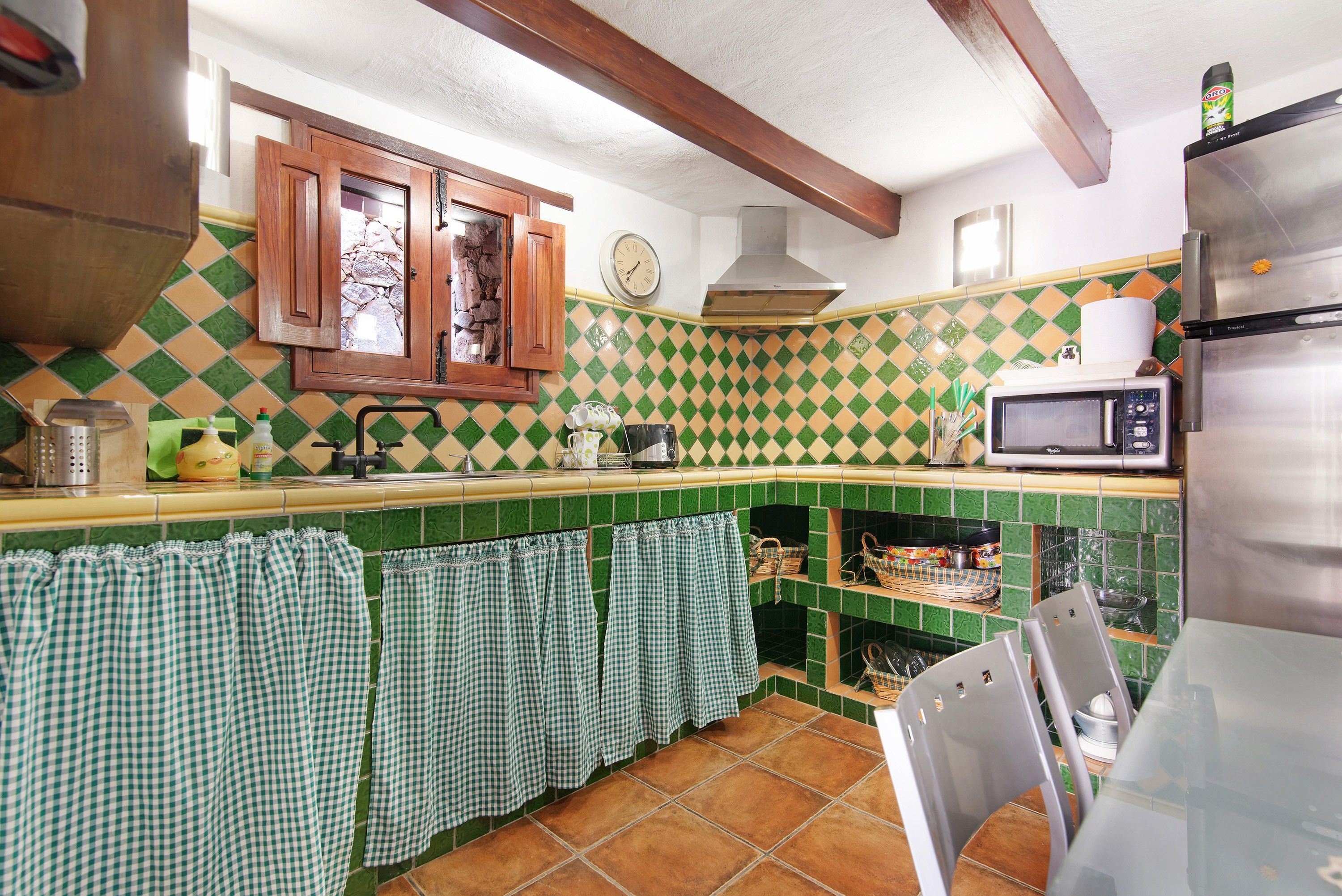 A kitchen with a green and white checkered backsplash, wooden cabinets, a stainless steel refrigerator, and a microwave.