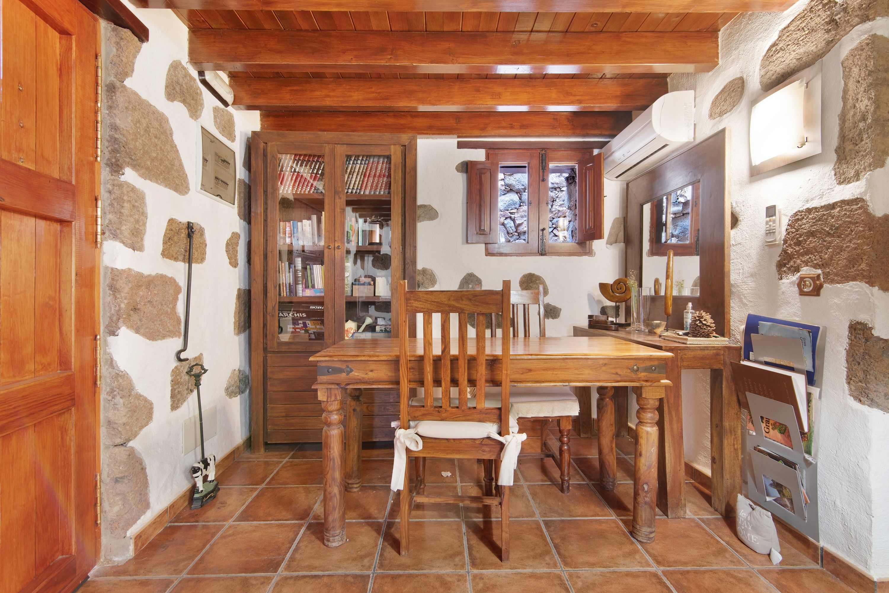 Ein rustikales Interieur mit einem Holztisch, Stühlen, einem Bücherregal und einer Steinwand.