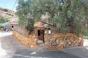 Un bâtiment en pierre avec une porte en bois, entouré d’oliviers.