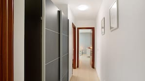 Un couloir avec un sol carrelé, une porte en bois et un mur blanc orné d’un tableau encadré.