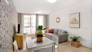 Un salon avec un canapé, une table à manger et des chaises, un téléviseur et une plante en pot.