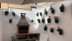 An outdoor patio with a brick oven, white chairs, and potted plants on the wall. - Holiday Home "Lola's Beach House" with Sea View, Private Pool & Wi-Fi (Calafell)