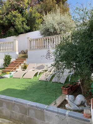 A garden with artificial grass, outdoor seating, a stone staircase, and a decorative fish statue. - Holiday Home "Lola's Beach House" with Sea View, Private Pool & Wi-Fi (Calafell)