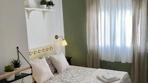 A bedroom with a bed, a bedside lamp, a shelf with plants, and a window with curtains. - Holiday Home "Lola's Beach House" with Sea View, Private Pool & Wi-Fi (Calafell)