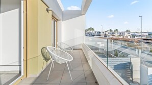 Ein Balkon mit zwei weißen Stühlen, einer Glastrennwand und Blick auf eine Wohngegend.
