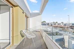 A balcony with two white chairs, a glass railing, and a view of a residential area.