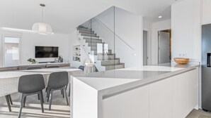 Eine moderne Küche mit Kochinsel, Essbereich mit Stühlen, einer Treppe und einem an der Wand befestigten Fernseher.