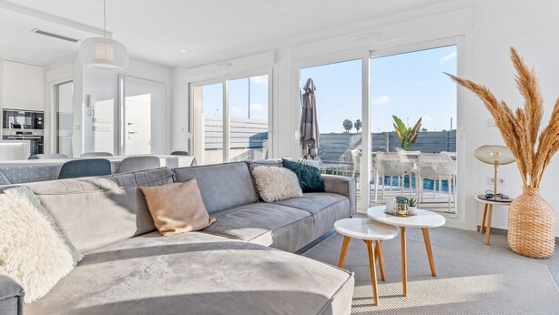 Ein modernes Wohnzimmer mit einem grauen Ecksofa, einem kleinen runden Tisch und einem großen Fenster mit Blick auf die Stadt.