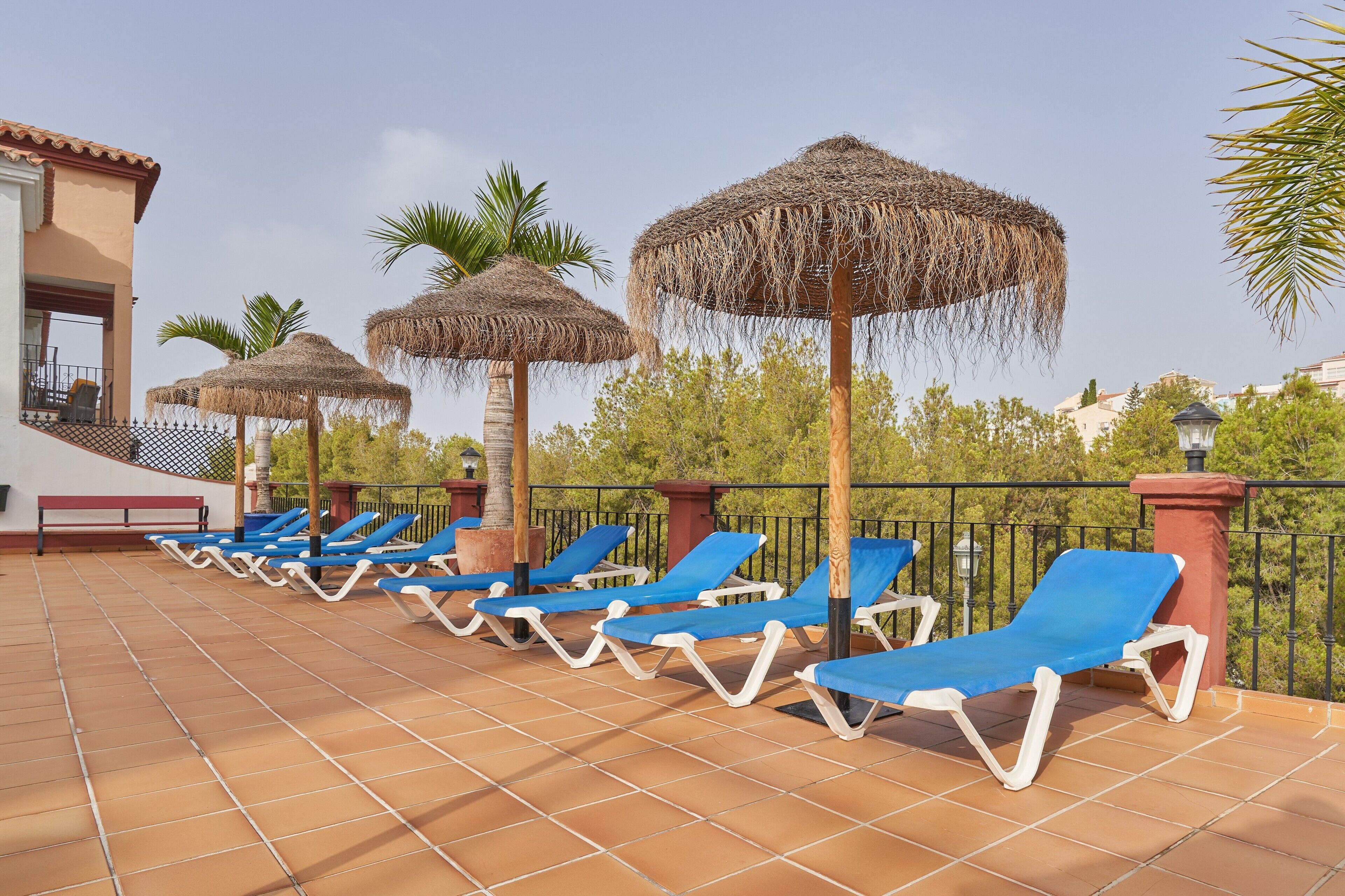 Terraço no telhado com espreguiçadeiras e guarda-sóis de palha.