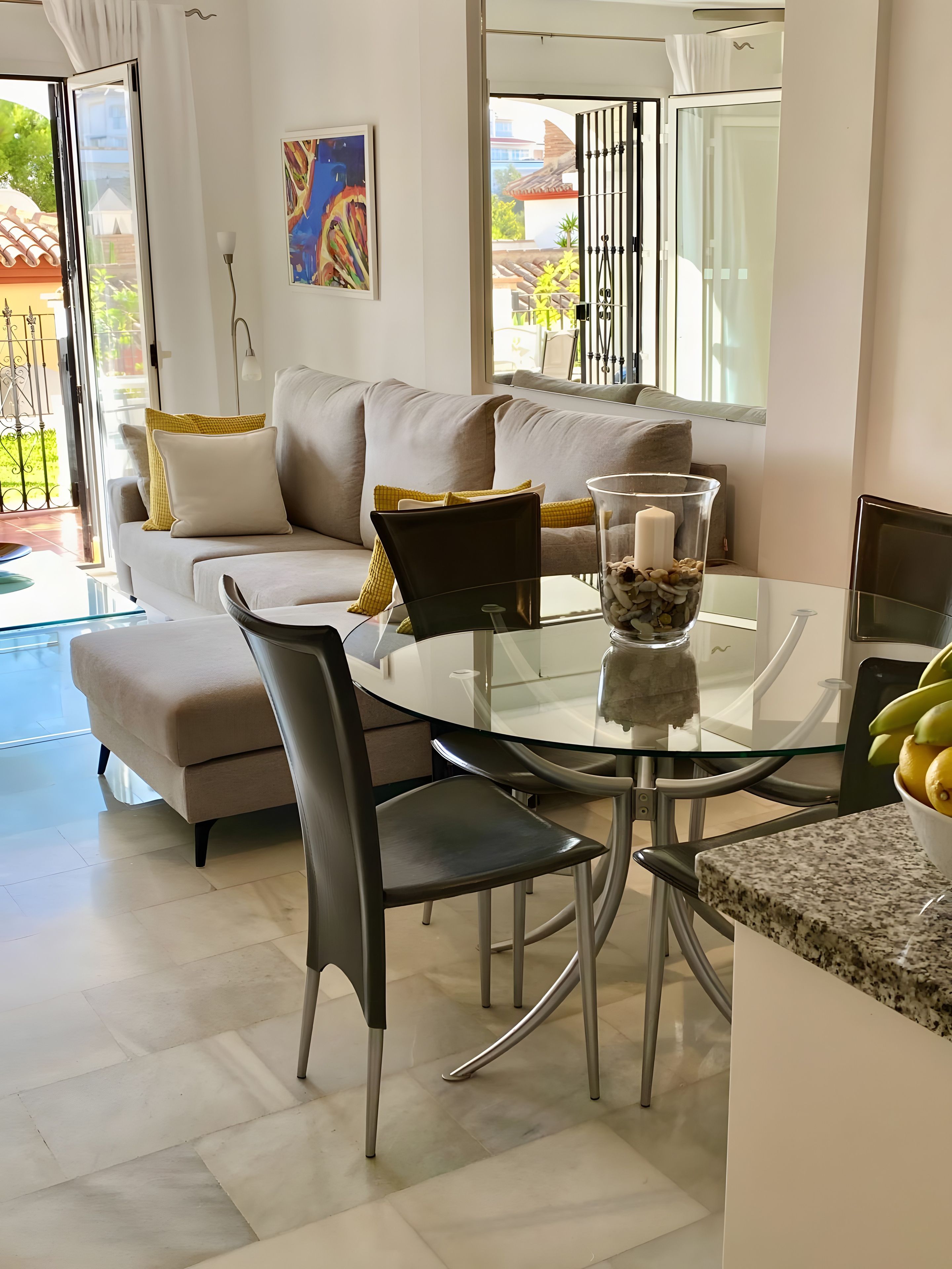 Una sala de estar moderna con una mesa de comedor de vidrio, un sofá con cojines y un cuadro en la pared.
