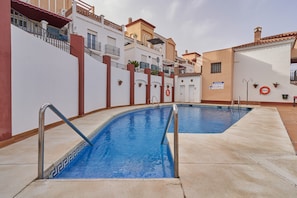 A swimming pool with a tiled edge and metal handrails, surrounded by a white wall with red accents and potted plants. - Apartment 'Superb  Nerja' with shared pool, Wi-Fi, Air-Con, near Burriana Beach (Nerja)