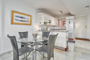 A modern kitchen with a glass dining table and chairs, white cabinets, and a stainless steel refrigerator. - Apartment 'Superb  Nerja' with shared pool, Wi-Fi, Air-Con, near Burriana Beach (Nerja)