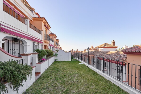 A residential area with a narrow pathway, white walls, and balconies with red railings.