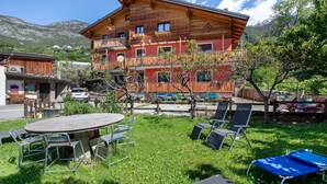 A wooden chalet with a balcony, a round table with chairs, and a grassy yard with lounge chairs. - Apartment "Casa Michod - Nonno Marcel" with Mountain View in Chatillon (Chatillon)