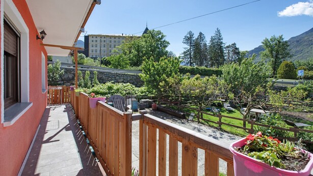 A balcony with a wooden railing, potted plants, and a view of a mountain and a building in the background. - Apartment "Casa Michod - Nonna Genia" with Mountain View, Shared Garden & Wi-Fi (Chatillon)