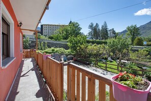 Un balcon doté d’une balustrade en bois, de plantes en pot et offrant une vue sur une montagne et un bâtiment situé au loin.