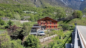 A mountain lodge with a red exterior, solar panels, and a white van parked in front. - Apartment "Casa Michod - Nonna Genia" with Mountain View, Shared Garden & Wi-Fi (Chatillon)
