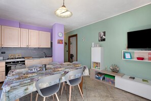Une cuisine de taille réduite avec des meubles en bois, une table à manger avec des chaises, une horloge et un téléviseur fixé au mur.