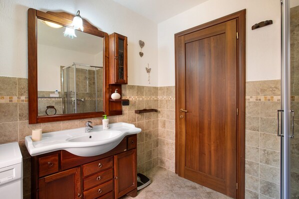 Une salle de bain avec un meuble-lavabo en bois, un évier, un miroir, une douche et une porte.