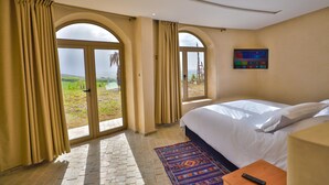 A hotel room with a large bed, a TV on the wall, and a view of the outdoors through arched windows. - Bhalil Farm House  (Bhalil)