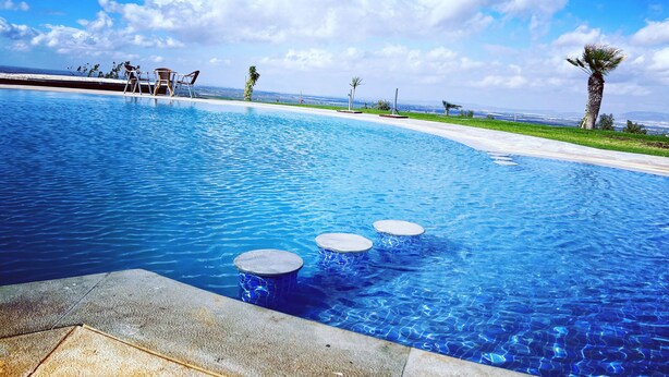 A clear blue pool with three circular steps leading into it, surrounded by a concrete deck. - Bhalil Farm House  (Bhalil)