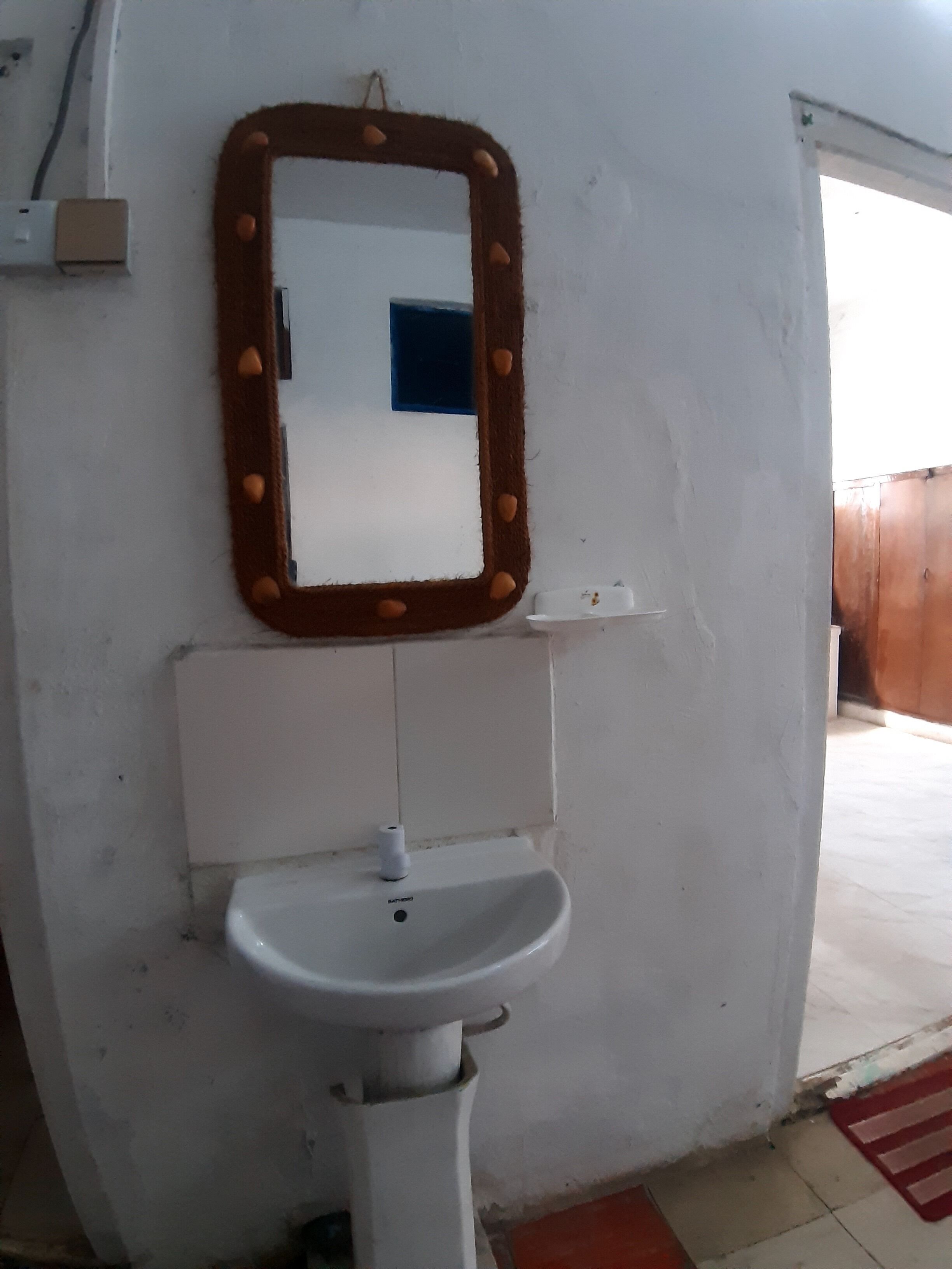 Ein Badezimmer mit einem weißen Waschbecken, einem Spiegel mit brauner Rahmen und einem blauen Fenster.