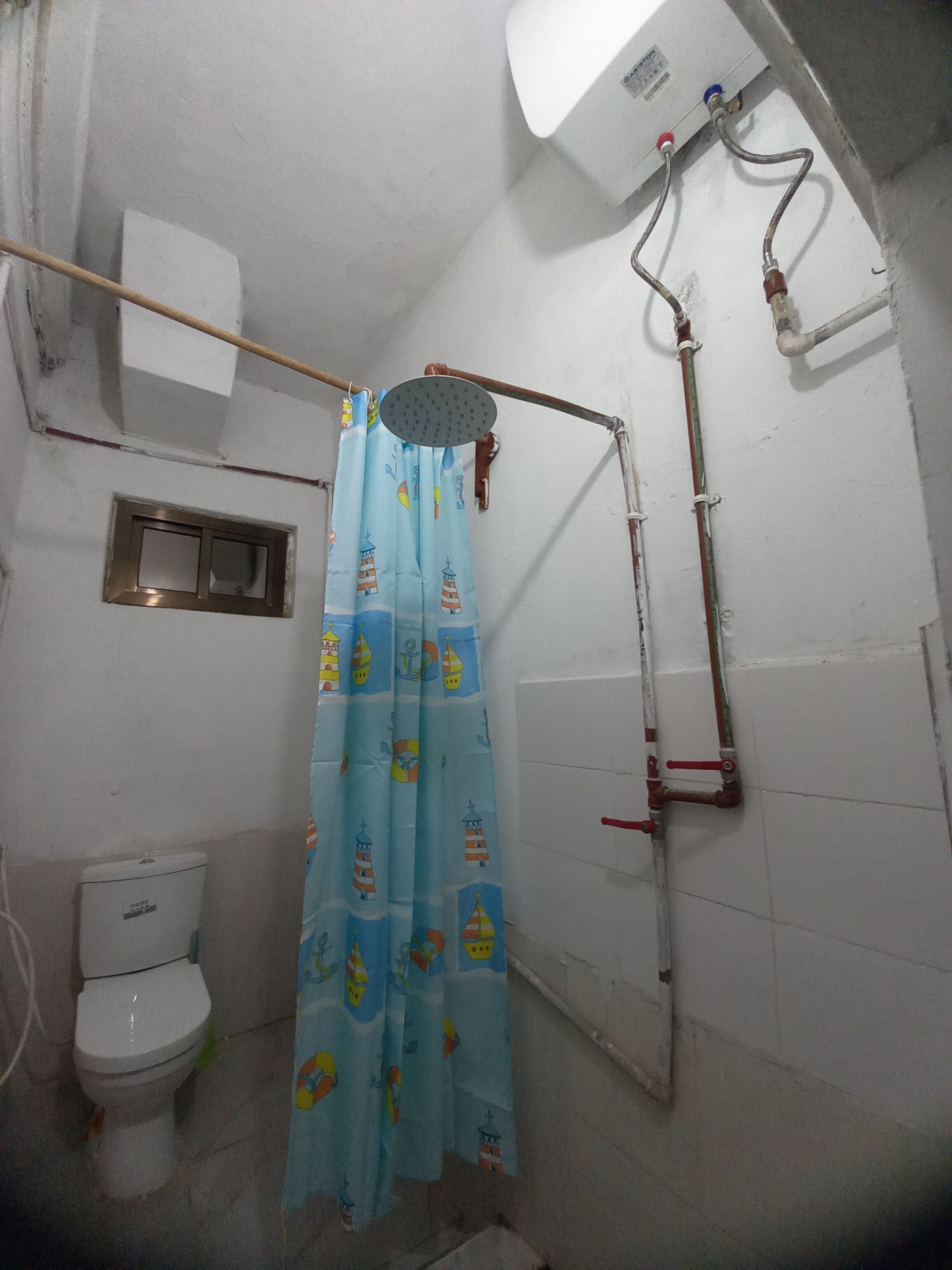 A small bathroom with a toilet, a shower curtain with a nautical theme, and visible plumbing.