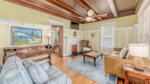 A spacious living room with a wooden ceiling, a fireplace, a cross on the wall, and a painting of a house. - THE BLUE HOUSE AT OLD COLORADO INN (Stuart)