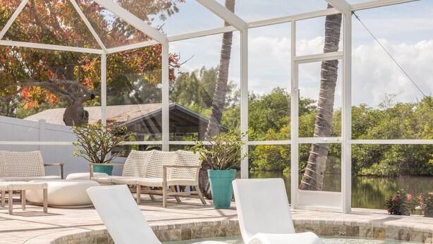 A pool area with lounge chairs and a hot tub, surrounded by large windows and potted plants.