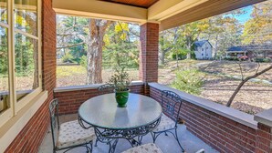 A covered patio with a round glass table and four chairs, a potted plant, and a view of a wooded area with houses in the background. - Near Downtown Cincinnati: Peaceful Retreat! (Cincinnati)