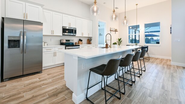 Une cuisine moderne avec des meubles blancs, des appareils en acier inoxydable et un îlot central doté de tabourets de bar.