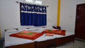 A double bed with white linens and two red blankets, a wooden headboard, and a blue curtain with white butterflies. - binay chapa homestay Jaldapara wildlife sanctuary best leving accommodation  (Madhya Madarihat)